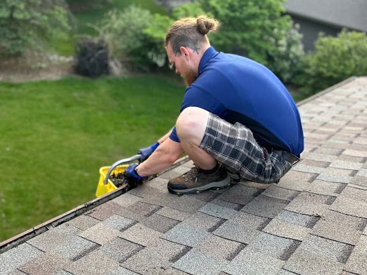 A Godvision Cleaning technician clearing a gutter by hand from the roofline, Battle Creek