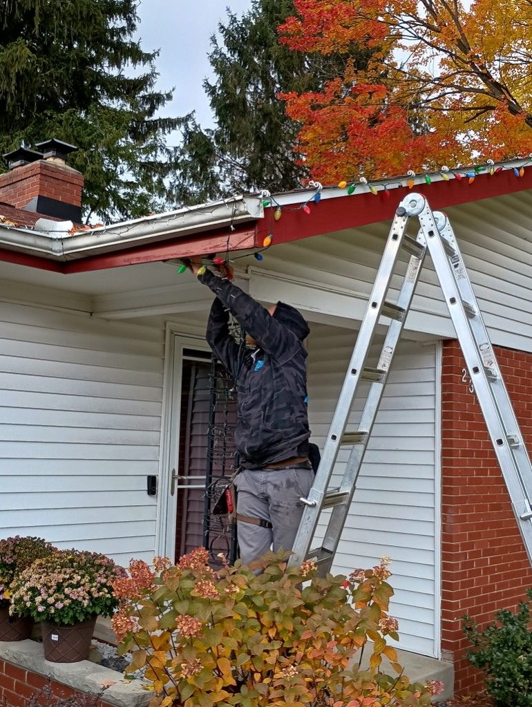A Godvision crew member on a ladder clearing the gutter line of a Battle Creek home under fall foliage