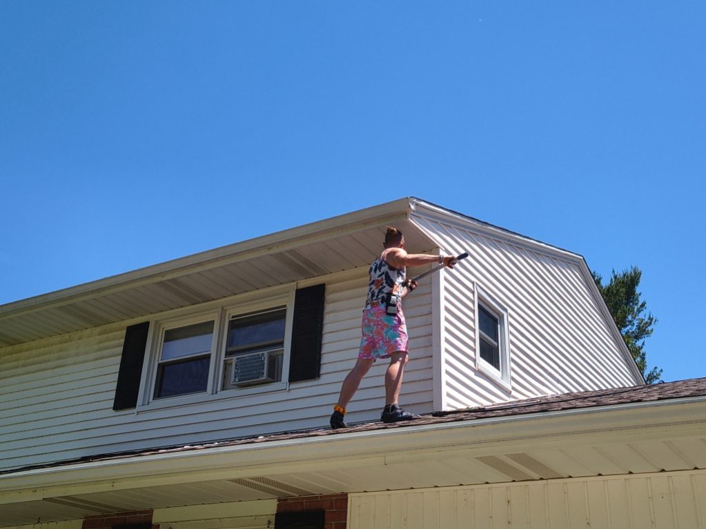 A Godvision crew member working a gutter line from the roof of a Battle Creek home