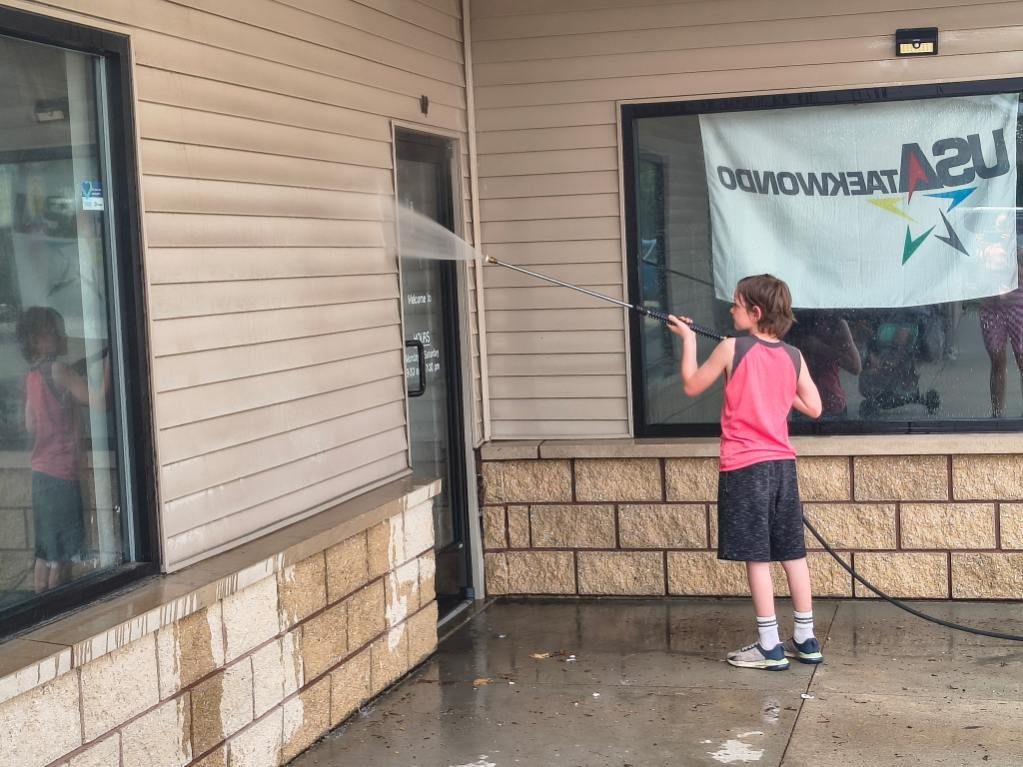 A young Godvision crew member washing the storefront glass at a taekwondo studio