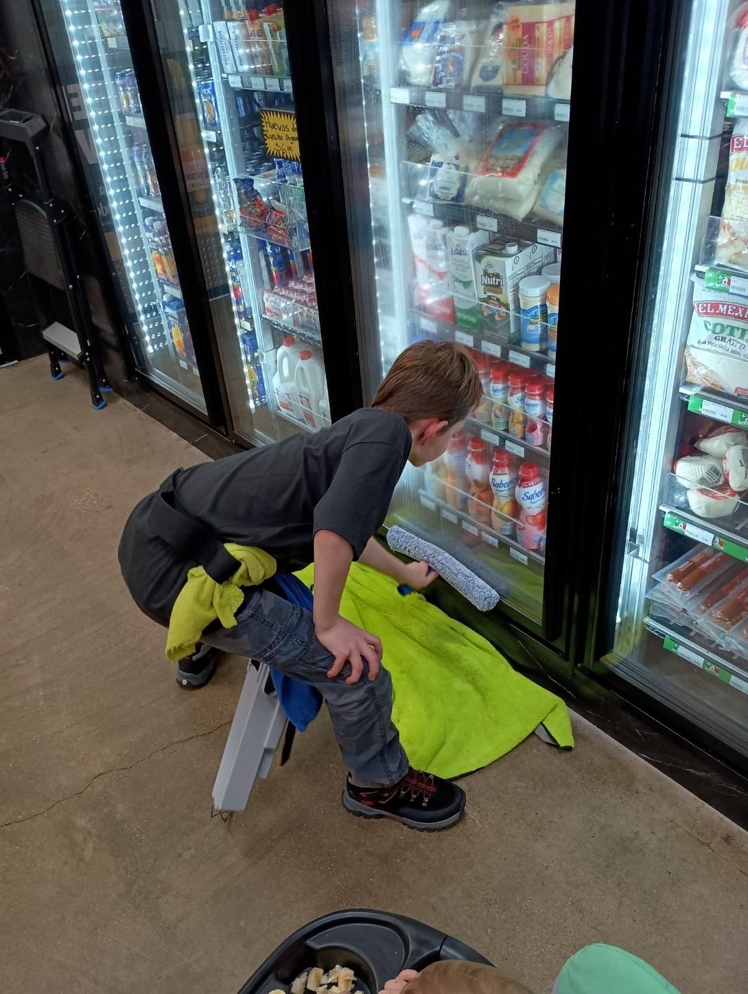 A young Godvision crew member cleaning the glass door of a drinks cooler on a janitorial job