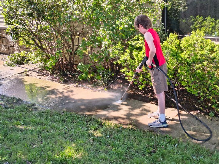 A young Godvision crew member rinsing down a lawn and planting beds on a Battle Creek job