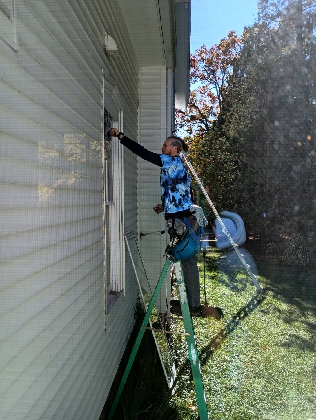 A Godvision Cleaning technician on a ladder washing an exterior window in a Godvision shirt